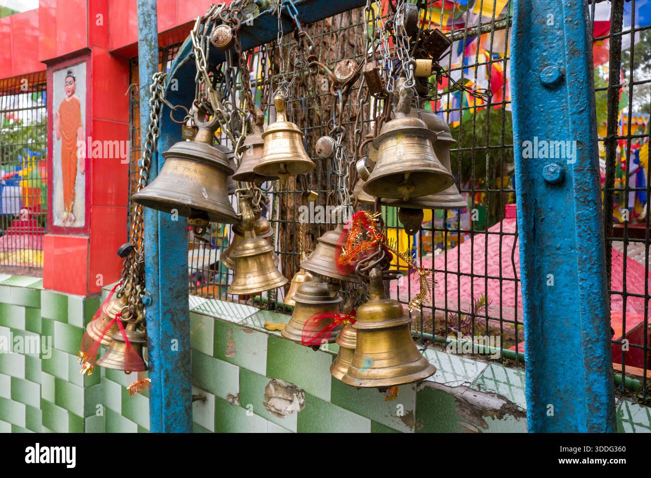 Gruppo di campane in ottone appese alle catene su un cancello blu intemprato al Tempio Mahakal, Darjeeling. Bandiere di preghiera colorate e pareti rosse del santuario creano un'atmosfera vivace e spirituale. Foto Stock