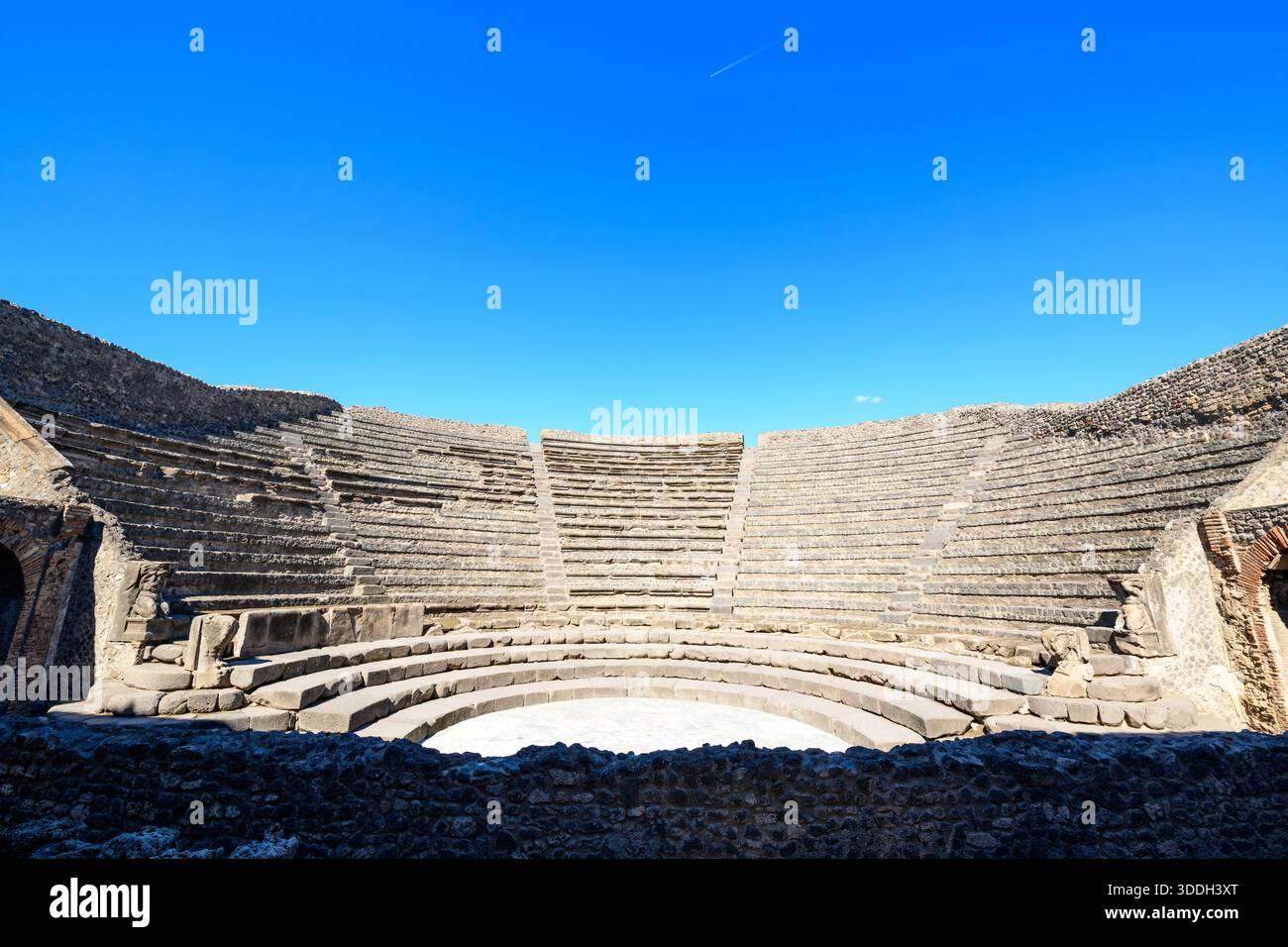 File semicircolari di posti a sedere in pietra intemprata formano lo storico piccolo teatro di Pompei, in Italia. La luce del sole mette in risalto le linee geometriche dell'anfiteatro contro un cielo vivido e senza nuvole. Foto Stock