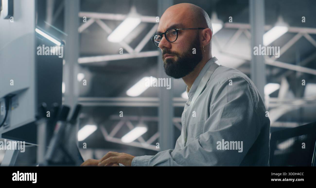 Specialista IT maschile con occhiali, incentrato sul monitor del computer. Caratteristiche di sfondo Cool, ambiente tecnico della sala di controllo dei server. Analisi dei dati critici e competenze dedicate. Foto Stock