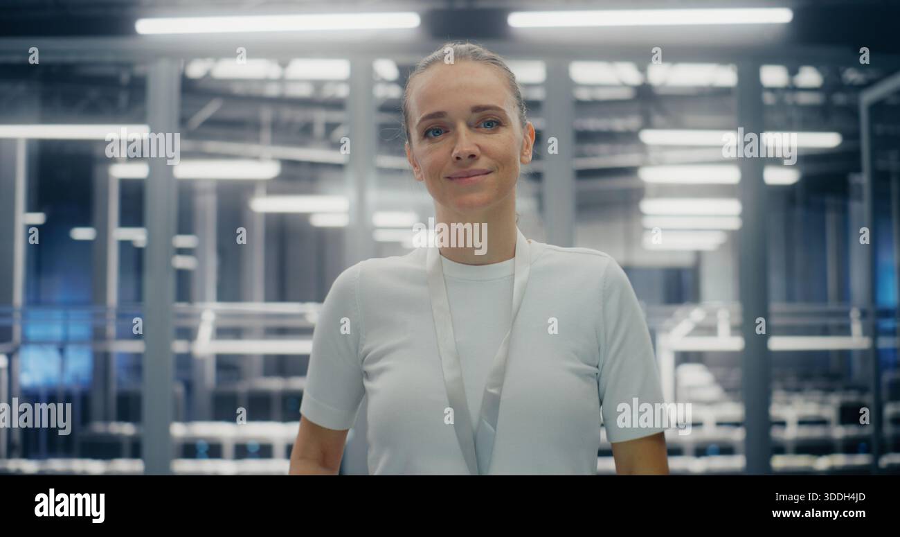 IT Infrastructure Professional, ingegnere dedicato che sorride calorosamente. Donna in piedi in una sala server su larga scala. Concetto di diversità di genere e successo nell'ambiente aziendale High Tech. Verticale. Foto Stock