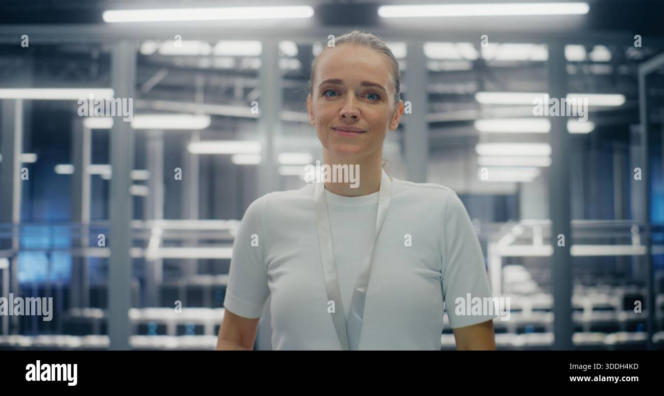 IT Infrastructure Professional, ingegnere dedicato che sorride calorosamente. Donna in piedi in una sala server su larga scala. Concetto di diversità di genere e successo nell'ambiente aziendale High Tech. Verticale. Foto Stock