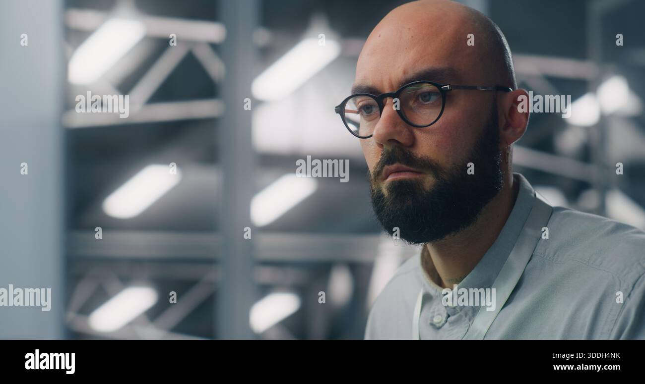 Primo piano di un ingegnere dedicato che supervisiona l'infrastruttura digitale di Workstation. Ambiente del data center ad alta sicurezza illuminato in blu visibile in modalità Soft Focus. Monitoraggio professionale e competenze tecniche. Foto Stock