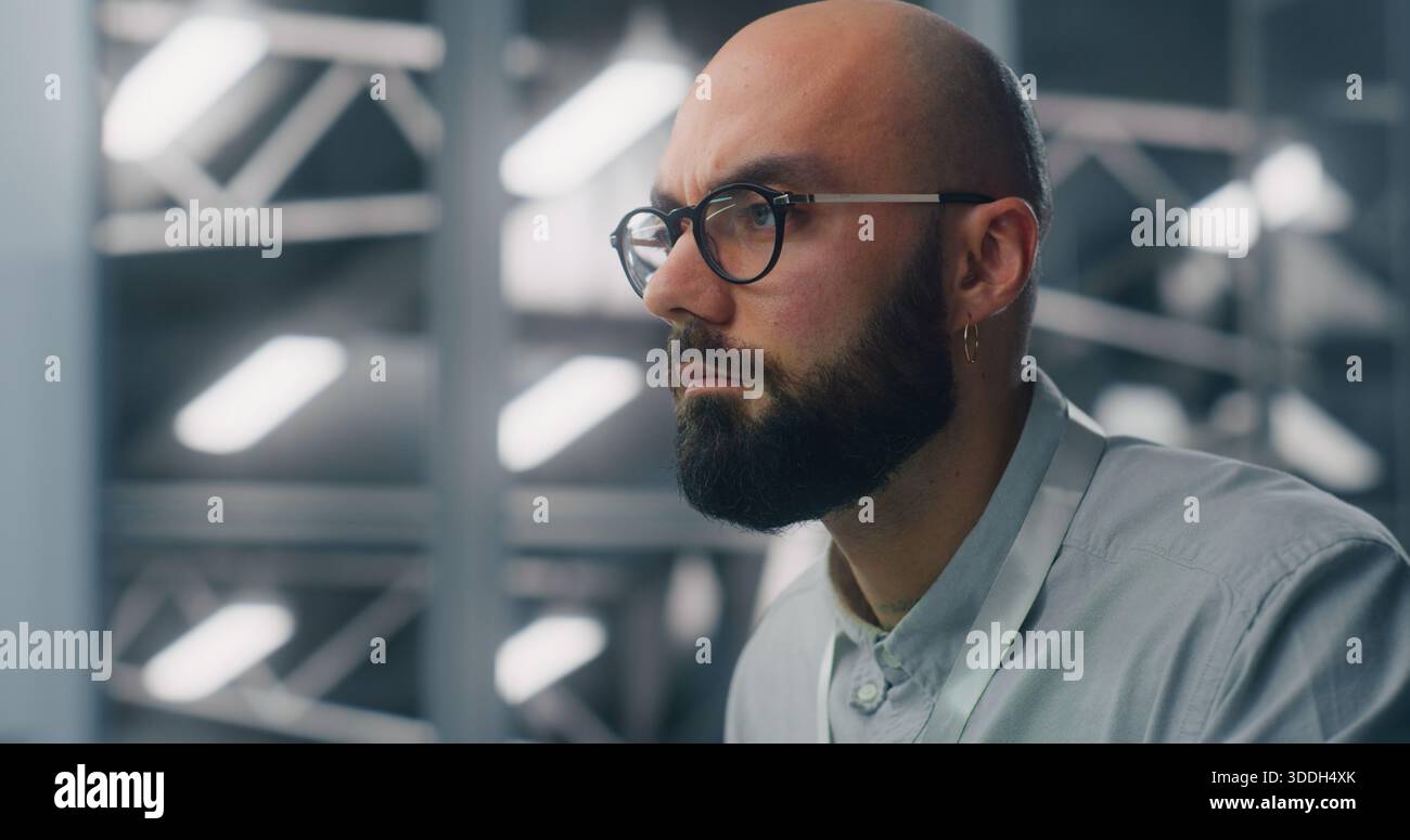 Primo piano di un ingegnere dedicato che supervisiona l'infrastruttura digitale di Workstation. Ambiente del data center ad alta sicurezza illuminato in blu visibile in modalità Soft Focus. Monitoraggio professionale e competenze tecniche. Foto Stock