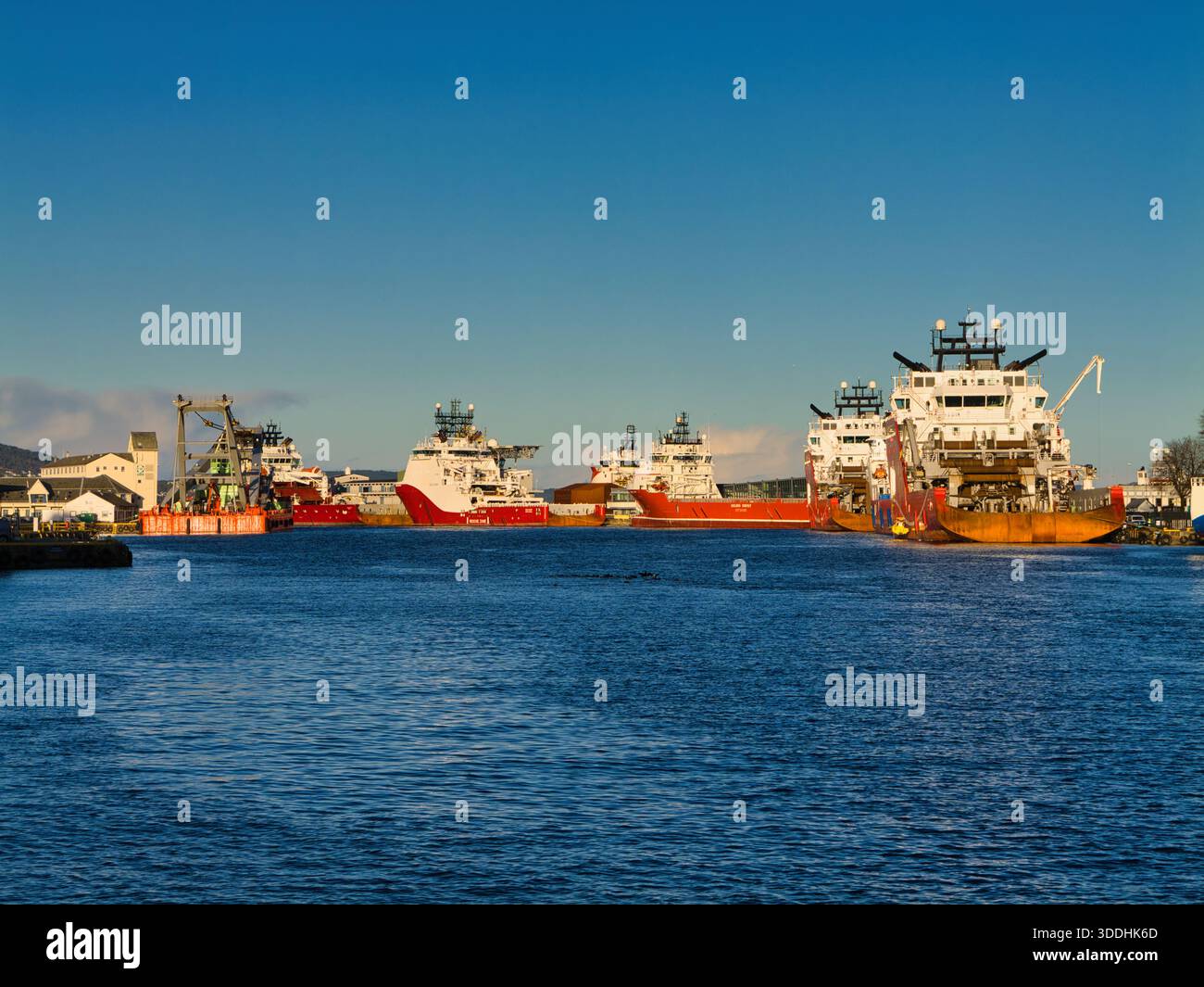 Bergen, Norvegia - 13 novembre 2025: Navi di servizio offshore e navi di rifornimento ormeggiate nel porto di Bergen, Norvegia, sotto cieli azzurri e con una calda luce mattutina sul lungomare. Foto Stock