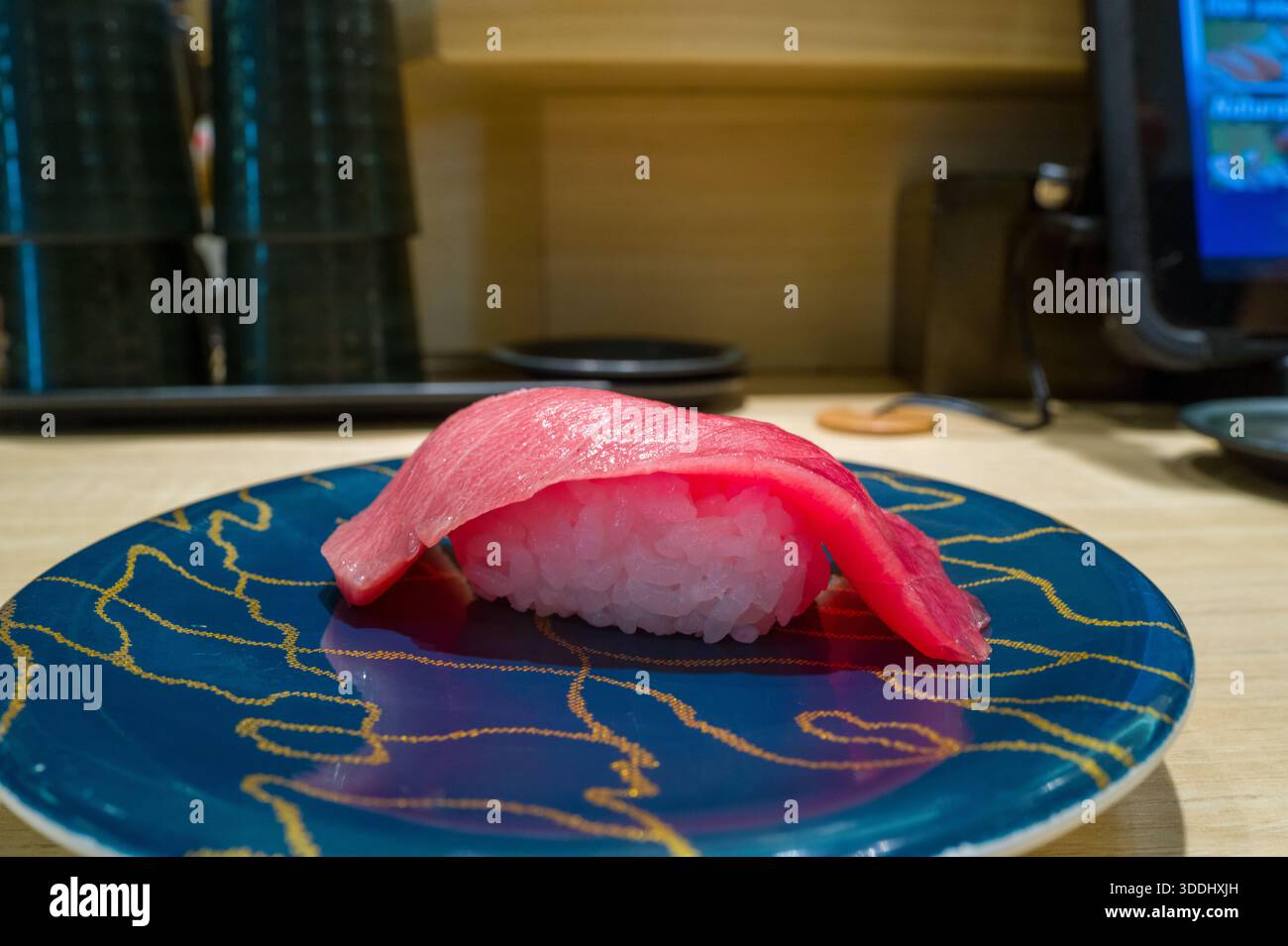 Un singolo pezzo di nigiri di tonno fresco e' posto elegantemente su un piatto blu lucido caratterizzato da motivi della linea d'oro, posto su un bancone di legno chiaro in un moderno ristorante di sushi ad Osaka. Foto Stock