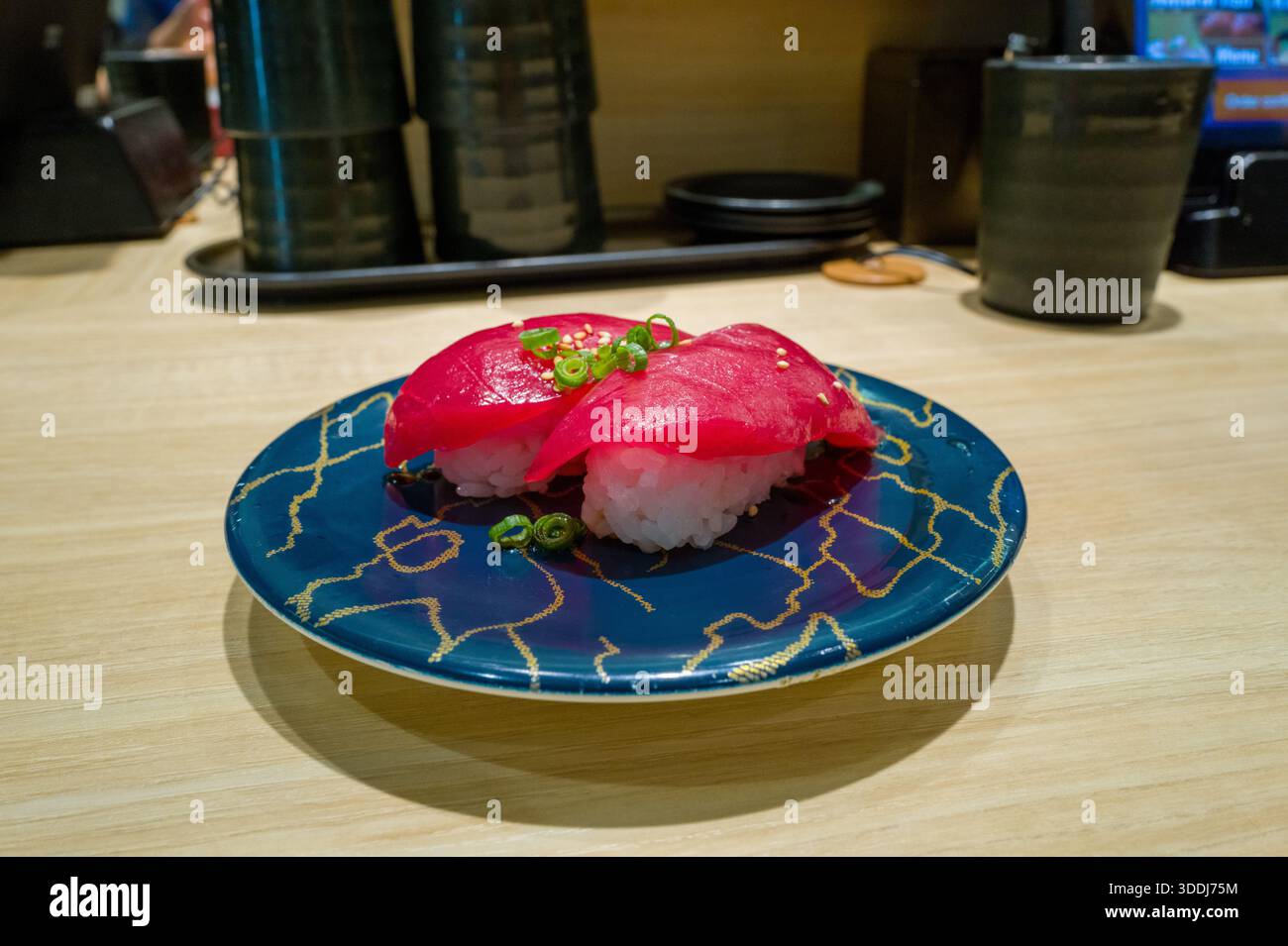 Fette luminose di tonno crudo riposano sopra il riso, guarnite con cipolle verdi e semi di sesamo, presentate su un piatto blu scuro con linee d'oro in un moderno ristorante giapponese. Foto Stock