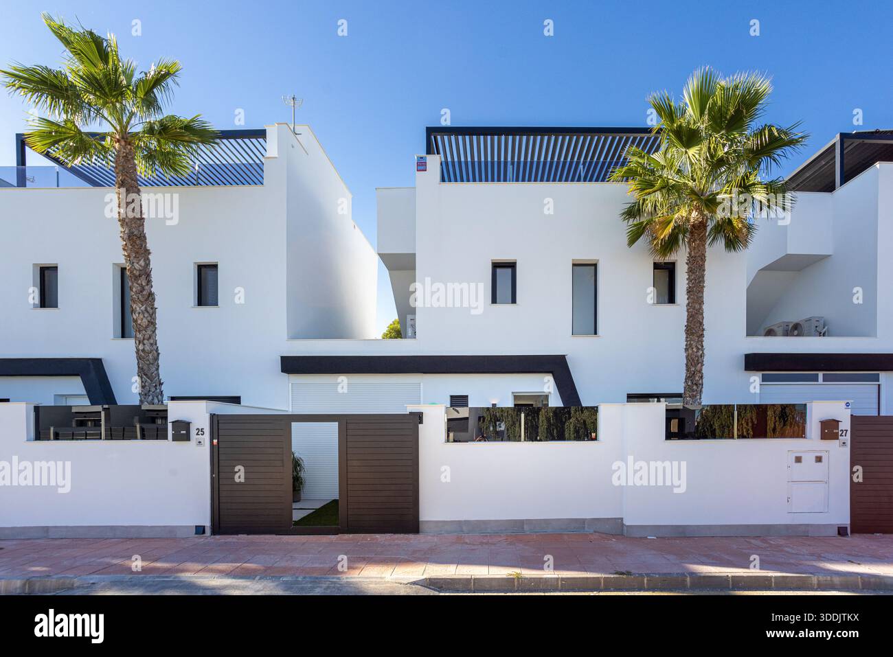 Architettura residenziale contemporanea con facciata bianca, accenti scuri, ingresso con cancello e paesaggio tropicale Foto Stock