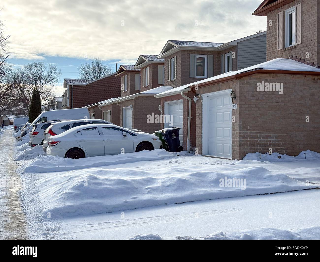 Strada residenziale nella Greater Toronto area. Fila di case di periferia in mattoni con auto coperte di neve nei vialetti. Fredda giornata invernale in Canada Foto Stock