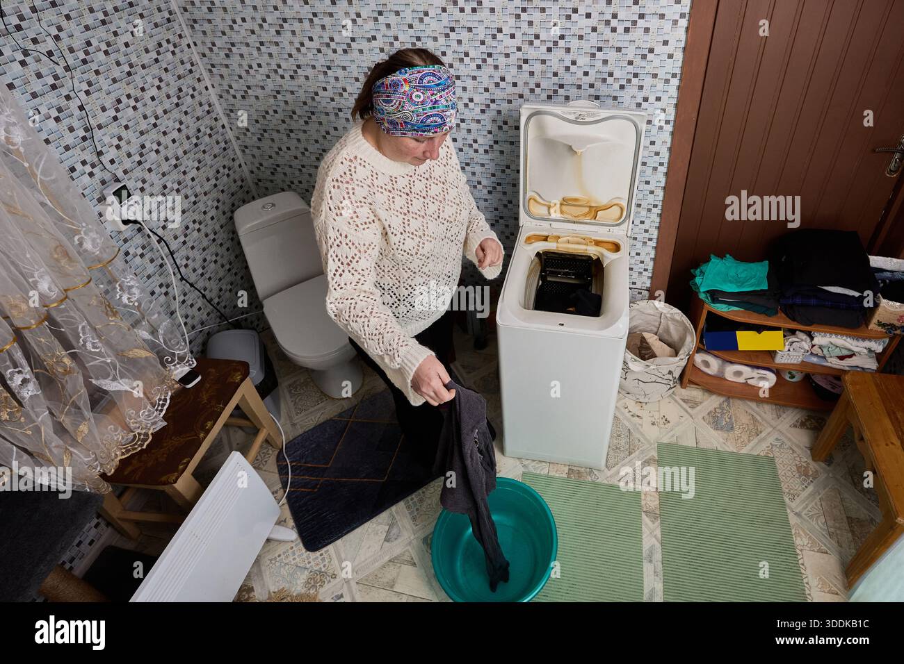 La lavanderia appena lavata viene prelevata dal tamburo della lavatrice automatica con caricamento superiore e spostata in un lavabo di plastica, la donna di circa 50 anni fa la casa Foto Stock