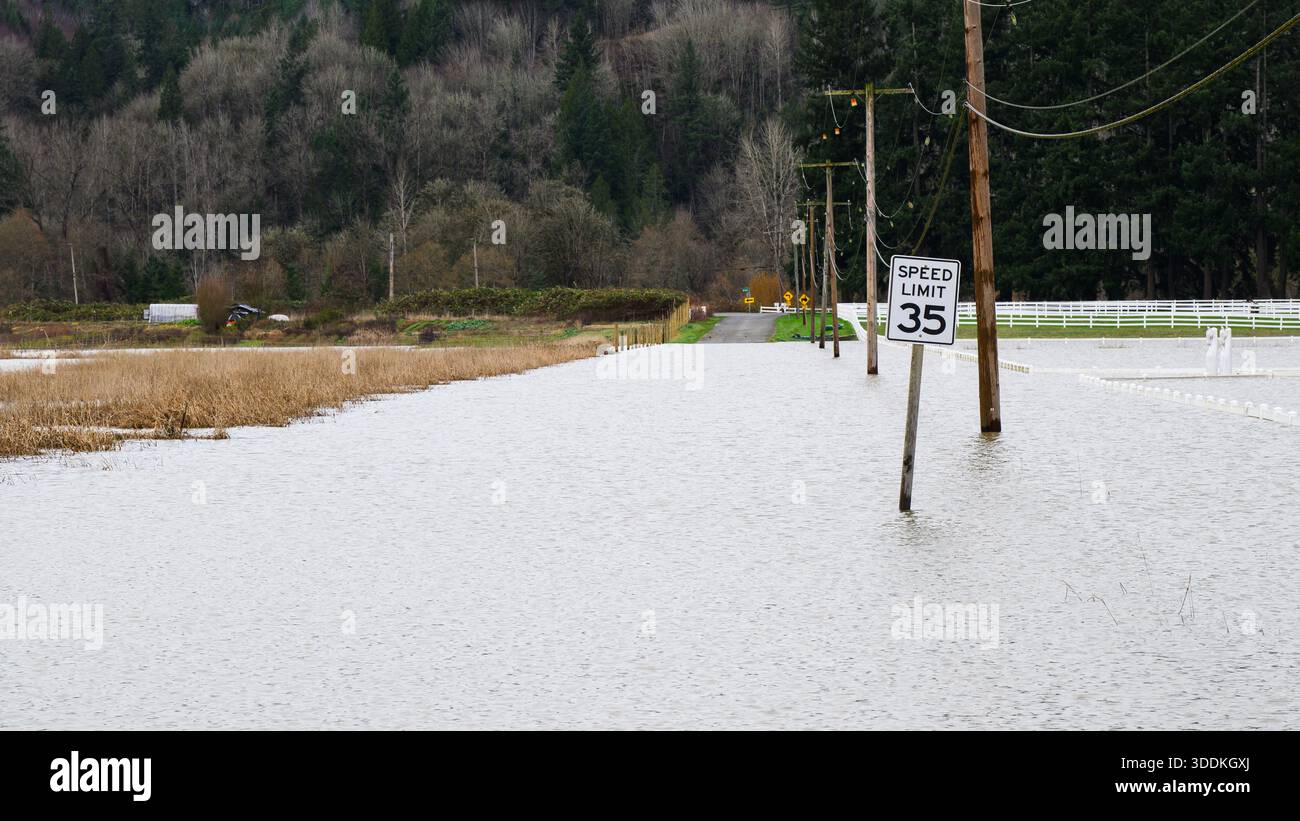 Inondazione rurale sommersa strada della contea con segnale di limite di velocità di 35 km/h in acqua Foto Stock