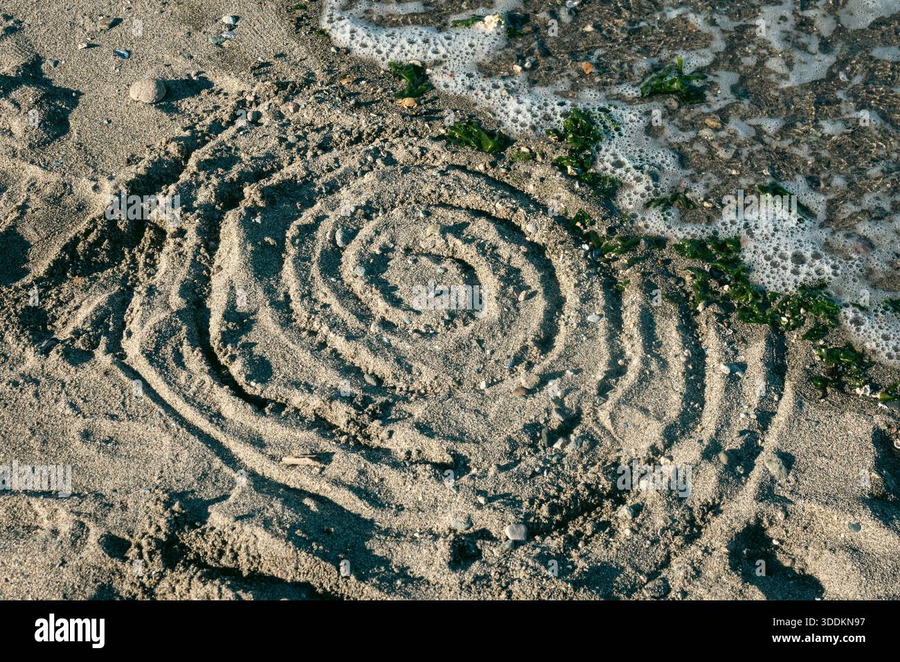 La marea scivola su una spirale disegnata nella sabbia sulla spiaggia di Vancouver, Canada Foto Stock