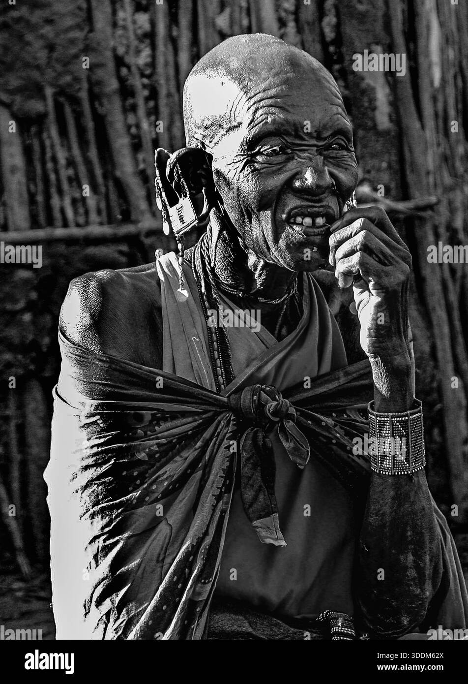 Una donna maasai anziana si rilassa e si allaccia fuori dalla sua capanna. Foto Stock