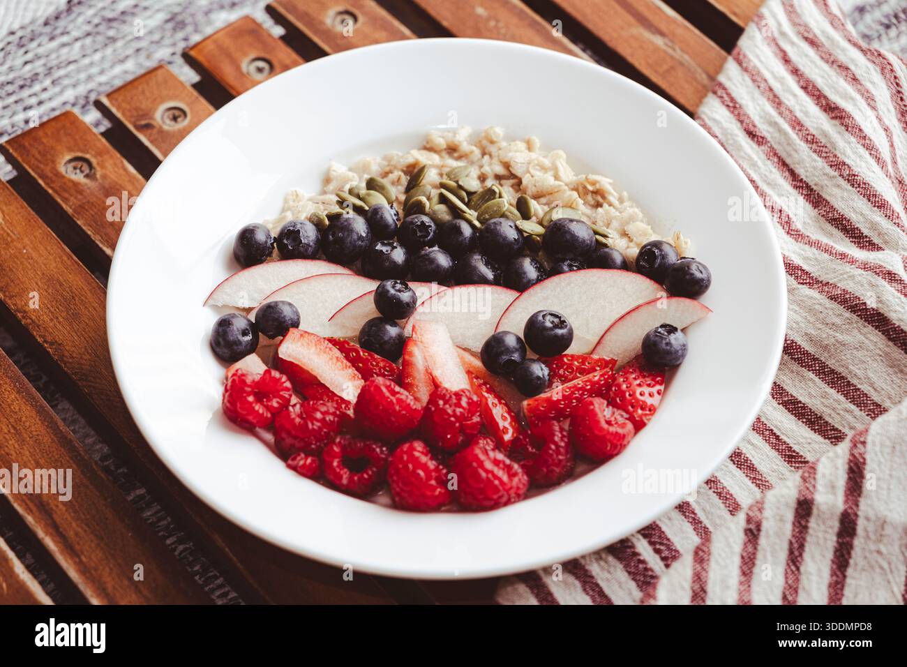 Una ciotola bianca in ceramica con farinata d'avena per colazione con fragole mirtilli e noci Foto Stock