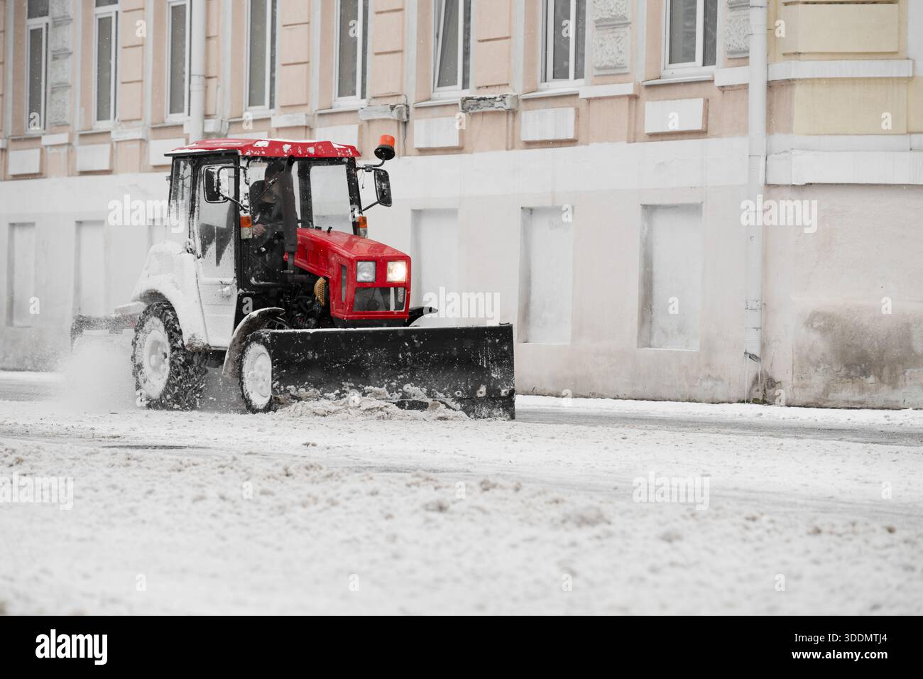 Vladikavkaz, Russia - 02 gennaio 2026 : trattore rosso brillante che rimuove la neve dal marciapiede con lama in acciaio . Foto Stock