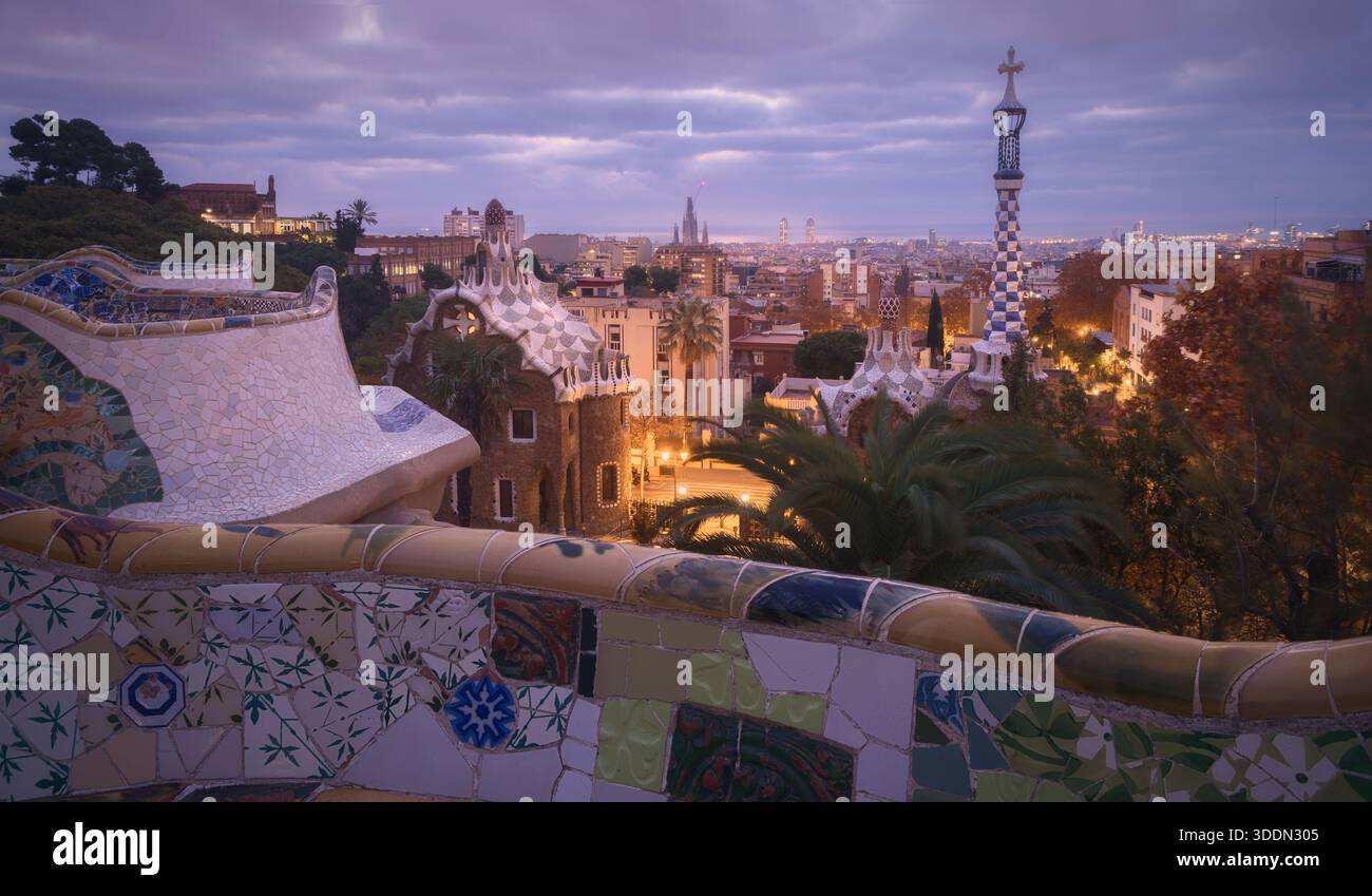 L'alba irrompe sul Parco Guell, illuminando i mosaici colorati e l'architettura unica, mentre la città si sveglia in un nuovo giorno nell'incantevole città di Barcellona Foto Stock