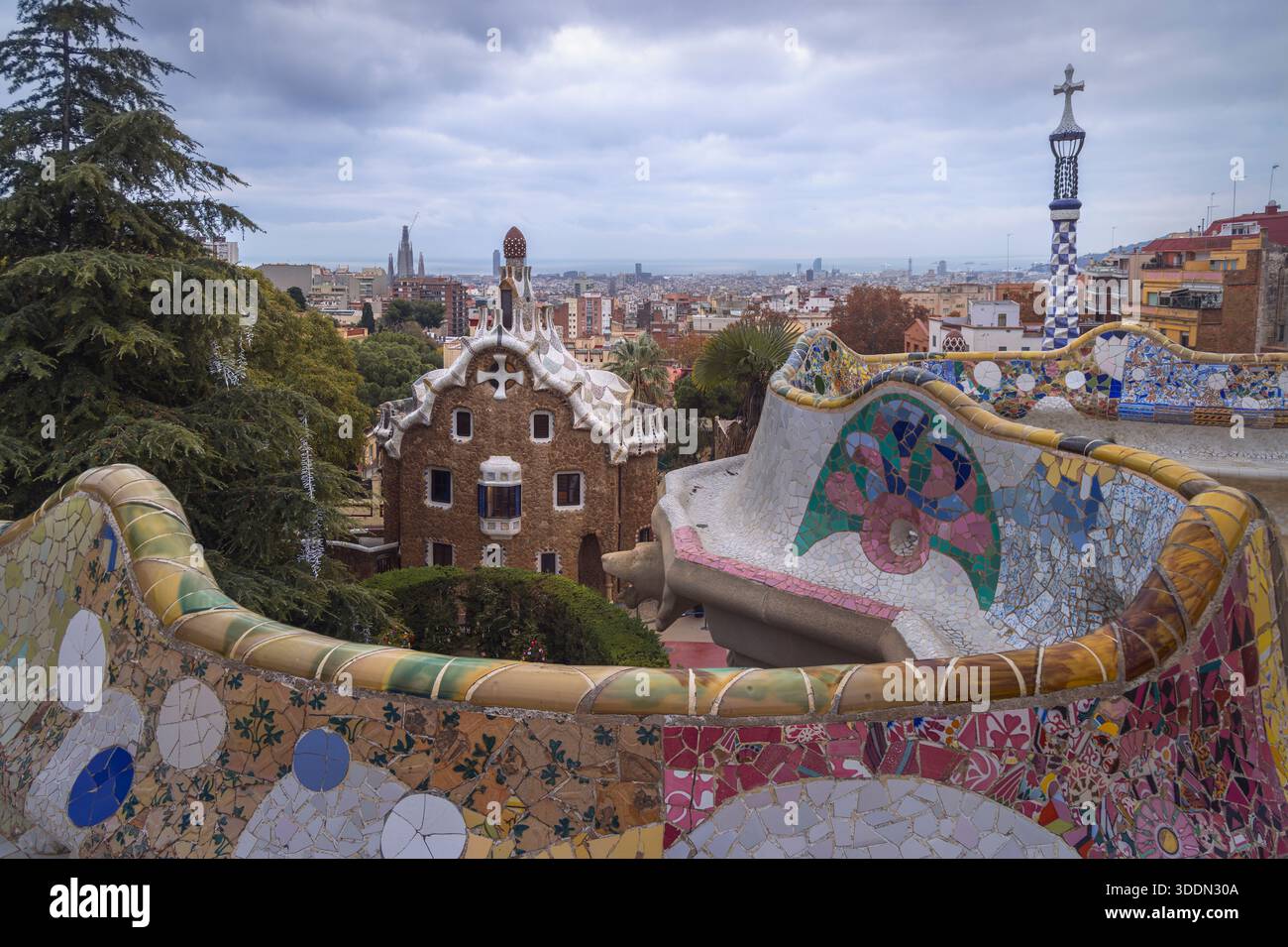 Mosaici colorati e architettura unica creano una scena magica al Park Guell. I visitatori ammirano la vista della città mentre sono circondati dal fascino della natura, B. Foto Stock