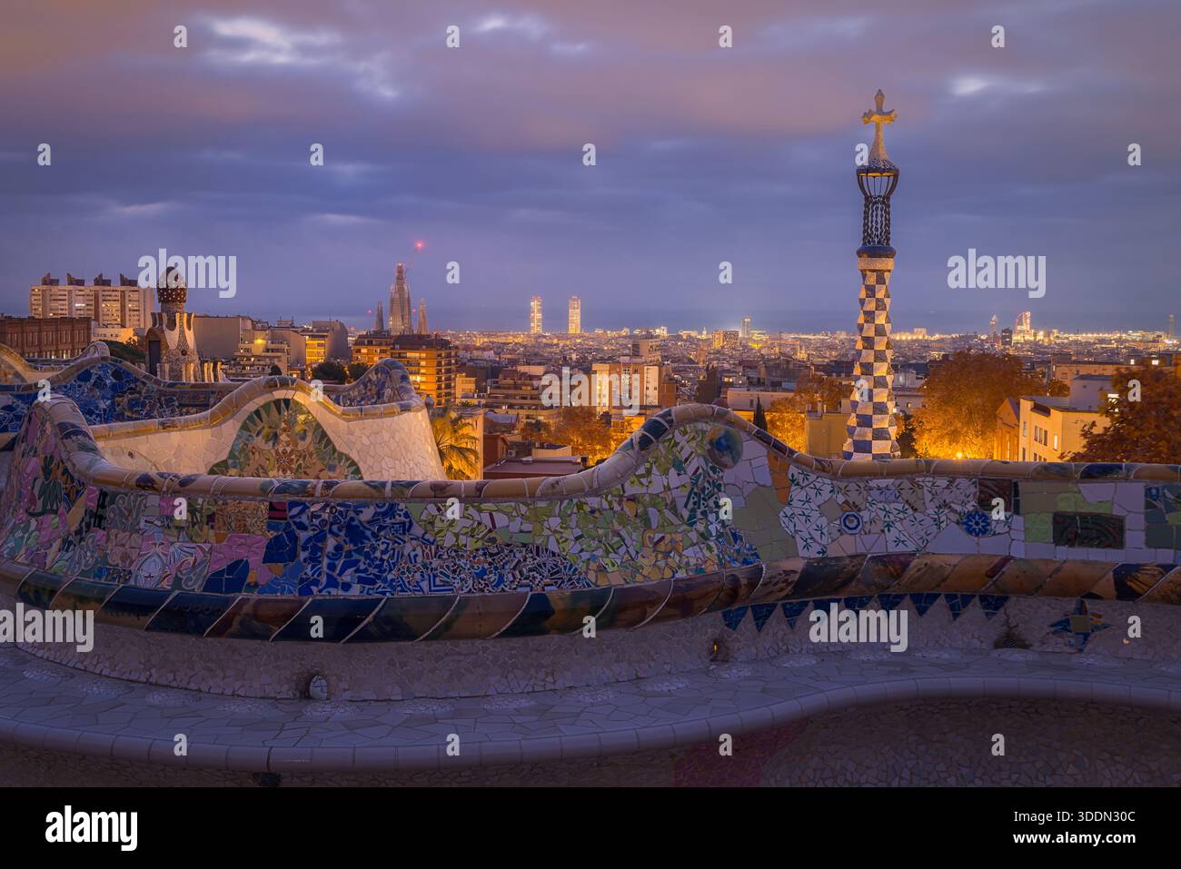 La luce soffusa del mattino bagna il Parco Guell, rivelando mosaici colorati e ampie vedute dello skyline di Barcellona, creando un'atmosfera tranquilla e incantevole Foto Stock