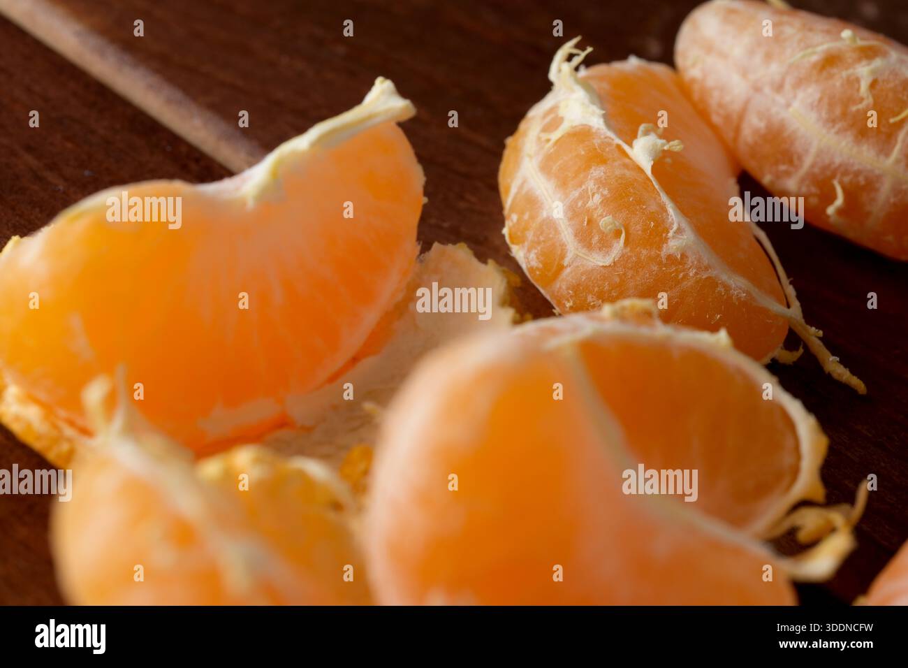 Fette di mandarino luminose disposte su un rustico tavolo in legno, invitante piacere. Foto Stock