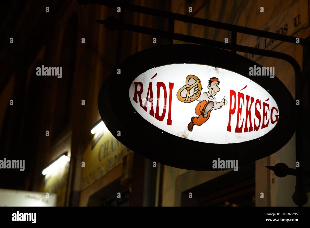 Cartello da forno illuminato per “Rádi Pékség” di notte a Eger, Ungheria, con un giocoso logo dei cartoni animati.Eger, Ungheria Foto Stock