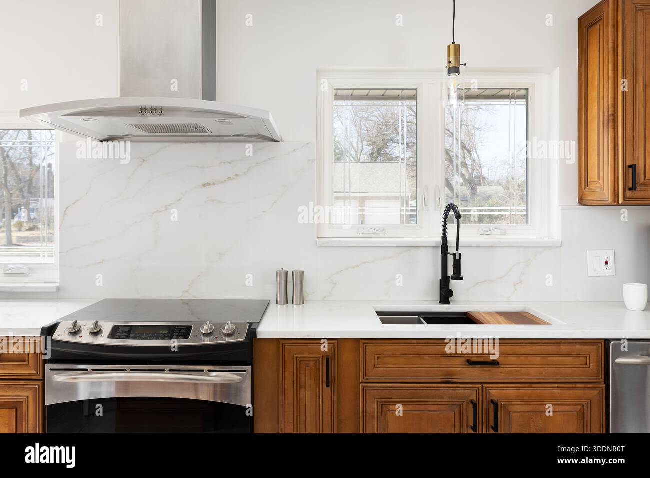 Cucina con piano cottura in acciaio inossidabile e cappuccio, lastra bianca di marmo calacatta e piano di appoggio bianco e armadi in legno. Foto Stock