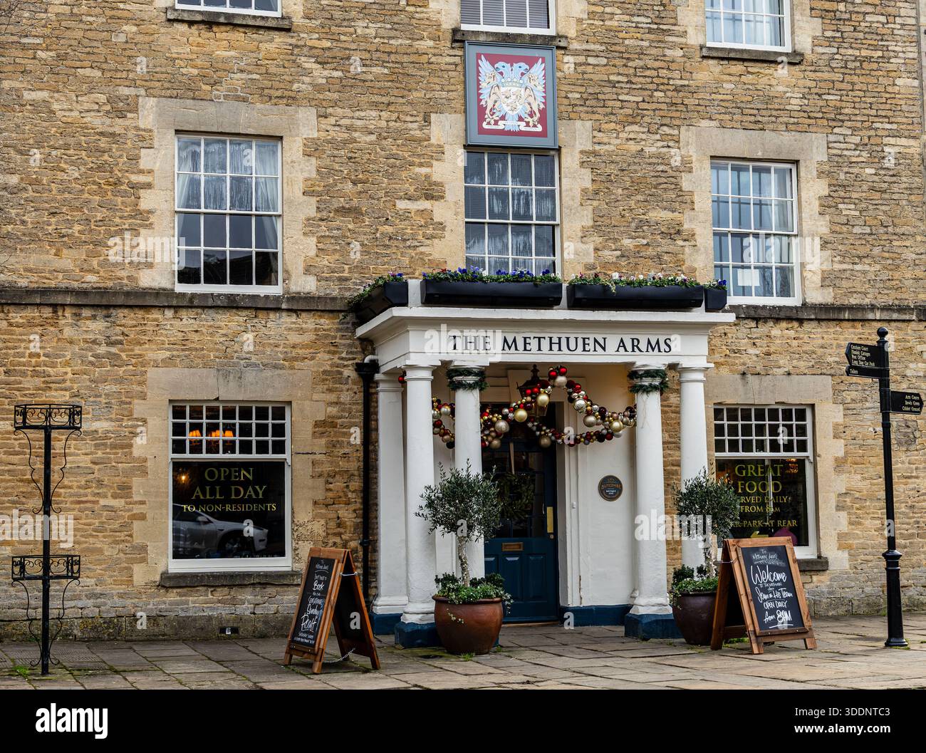 Edificio storico in pietra con colonne che ospita il pub Methuen Arms Corsham Wiltshire decorato con ghirlande e segnaletica all'aperto in una giornata nuvolosa Foto Stock