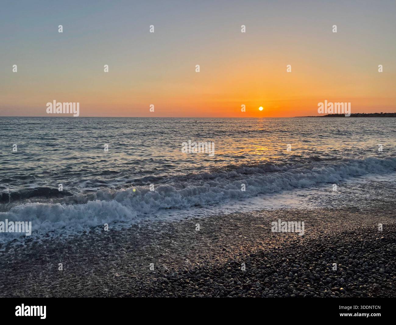 Tramonto sul mare calmo con onde dolci e spiaggia di ciottoli Foto Stock