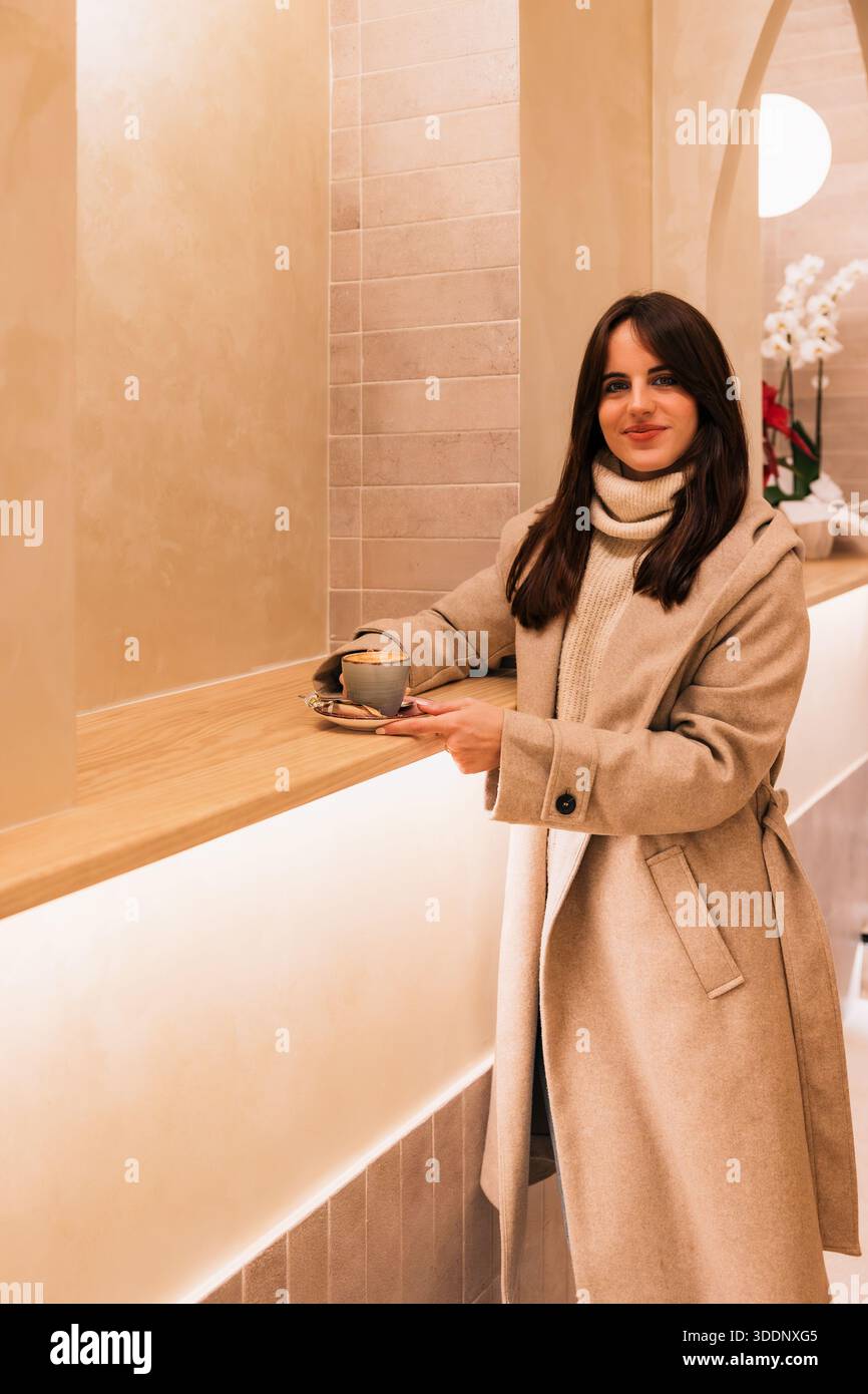 Giovane donna che si gusta un caffè in un accogliente e moderno bar interno Foto Stock