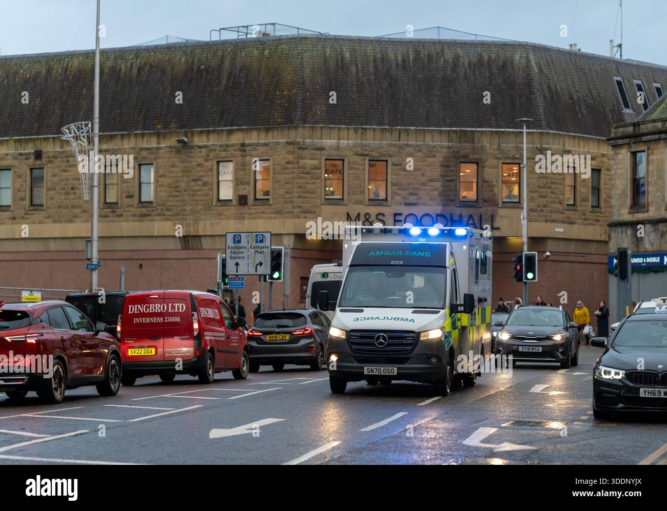 Un'ambulanza con i suoi semafori lampeggianti si dirige attraverso il traffico nel centro di Inverness. Le auto si fermano per cedere mentre si dirige verso una chiamata urgente duri Foto Stock