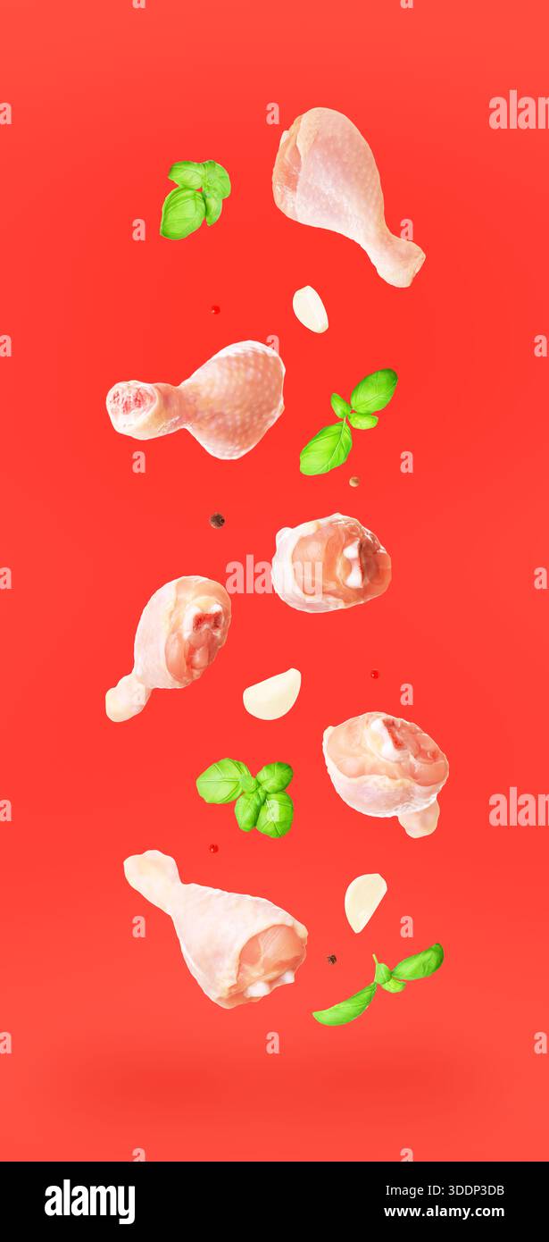 Cosce di pollo crudo volante con basilico fresco, aglio e spezie isolate su sfondo rosso. Concetto creativo di levitazione del cibo. Foto di alta qualità Foto Stock