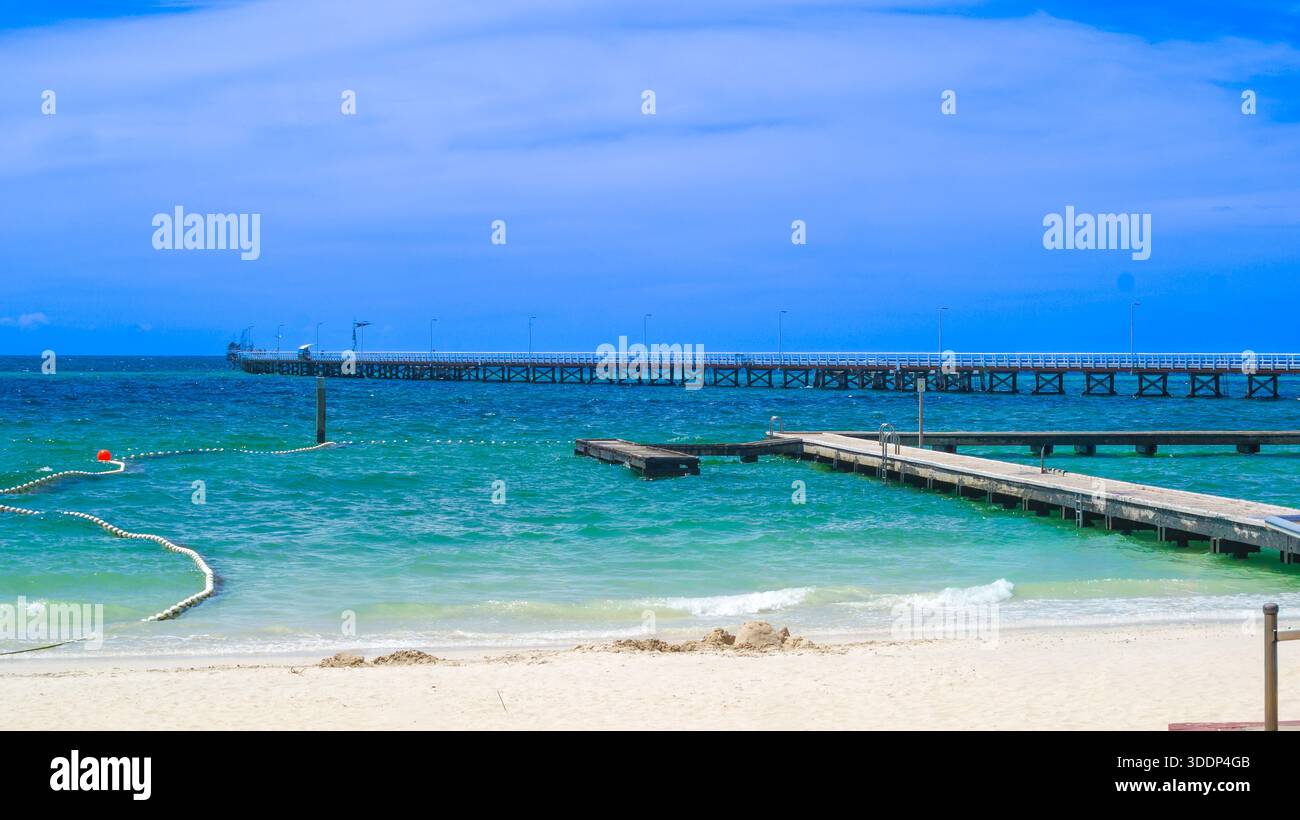 Un lungo molo in legno si estende nell'oceano turchese, circondato da spiaggia sabbiosa e cielo limpido, evocando relax e serenità. Foto Stock