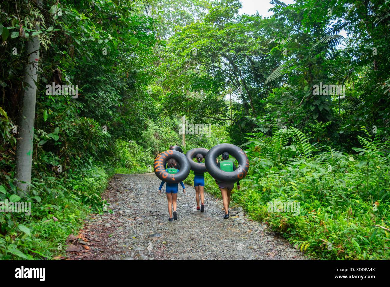 Gruppo di giovani che trasportano tubi gonfiabili lungo un sentiero a San Cipriano, Valle del Cauca, Colombia, immerso nel verde. Foto Stock