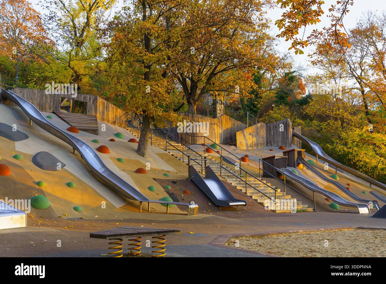 Colorato parco giochi all'aperto con aree per arrampicate e design moderno in un pomeriggio primaverile. Incredibili alberi di colore autunnale sullo sfondo Foto Stock