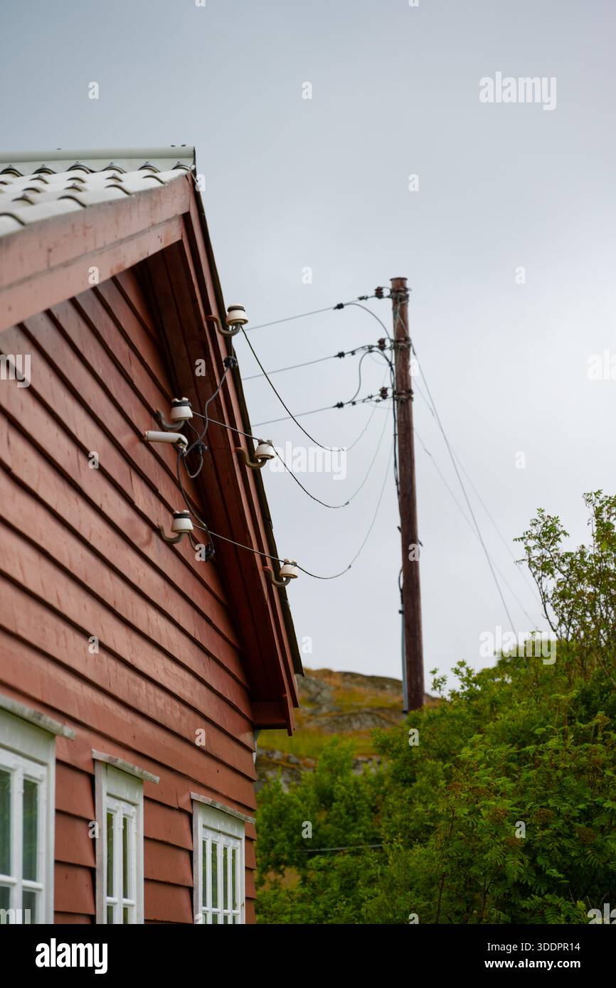 Linee elettriche da un palo a una casa di legno rossa Foto Stock