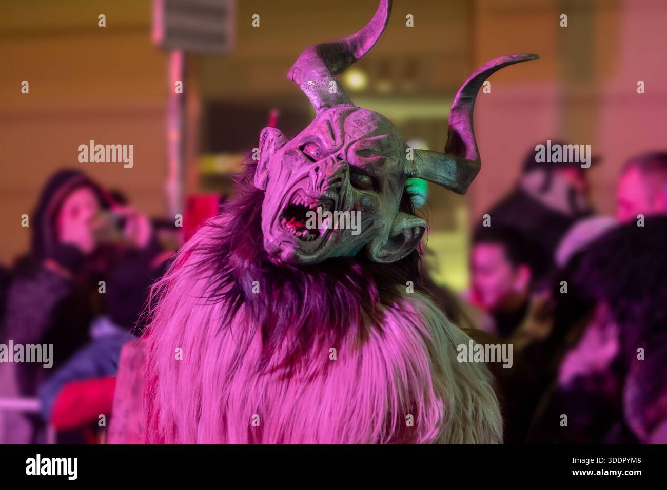 Un krampus con corna è illuminato con luce rosa durante la processione del festival Foto Stock