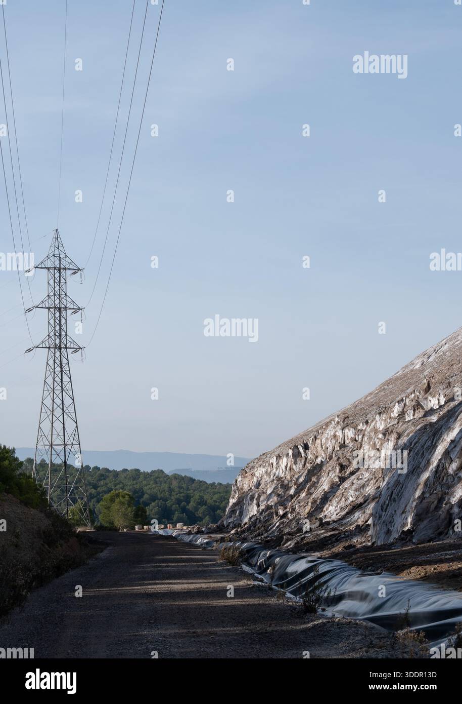Una vasta montagna di sale industriale si infila accanto a un pilone della linea elettrica, simboleggiando immense risorse, sfide ambientali e soluzioni sostenibili. A r Foto Stock