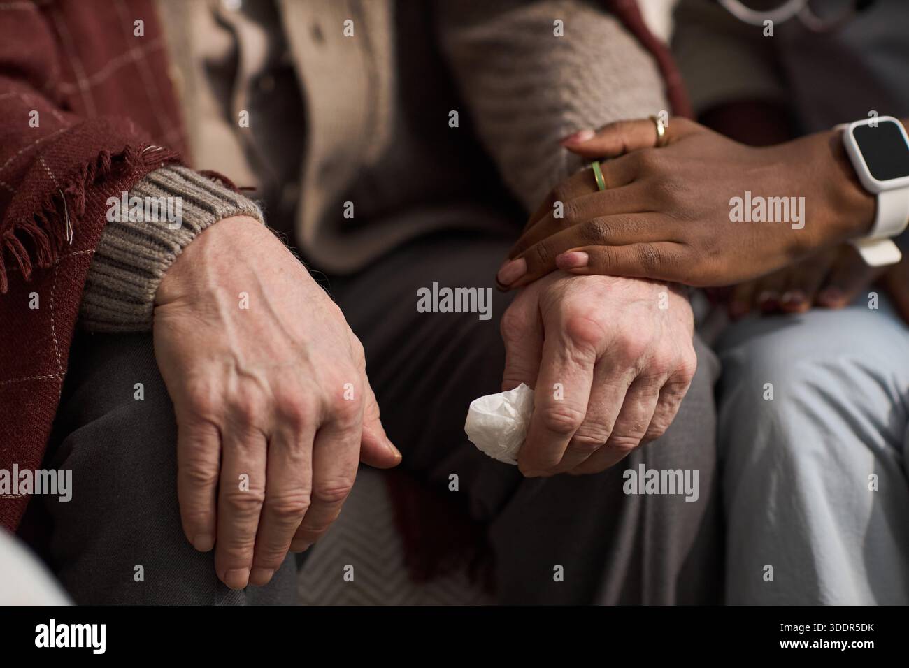 Anziano uomo caucasico seduto con le mani appoggiate sulle ginocchia, tenendo i tessuti, viene confortato dalla giovane donna nera che mette delicatamente la mano sulla sua, mostrando sostegno ed empatia Foto Stock
