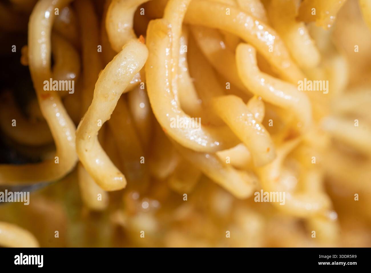 Primo piano di tagliatelle ricci gialle cotte. Delizioso sfondo con texture ramen per l'industria alimentare, il design del menu e la cucina asiatica. Foto Stock