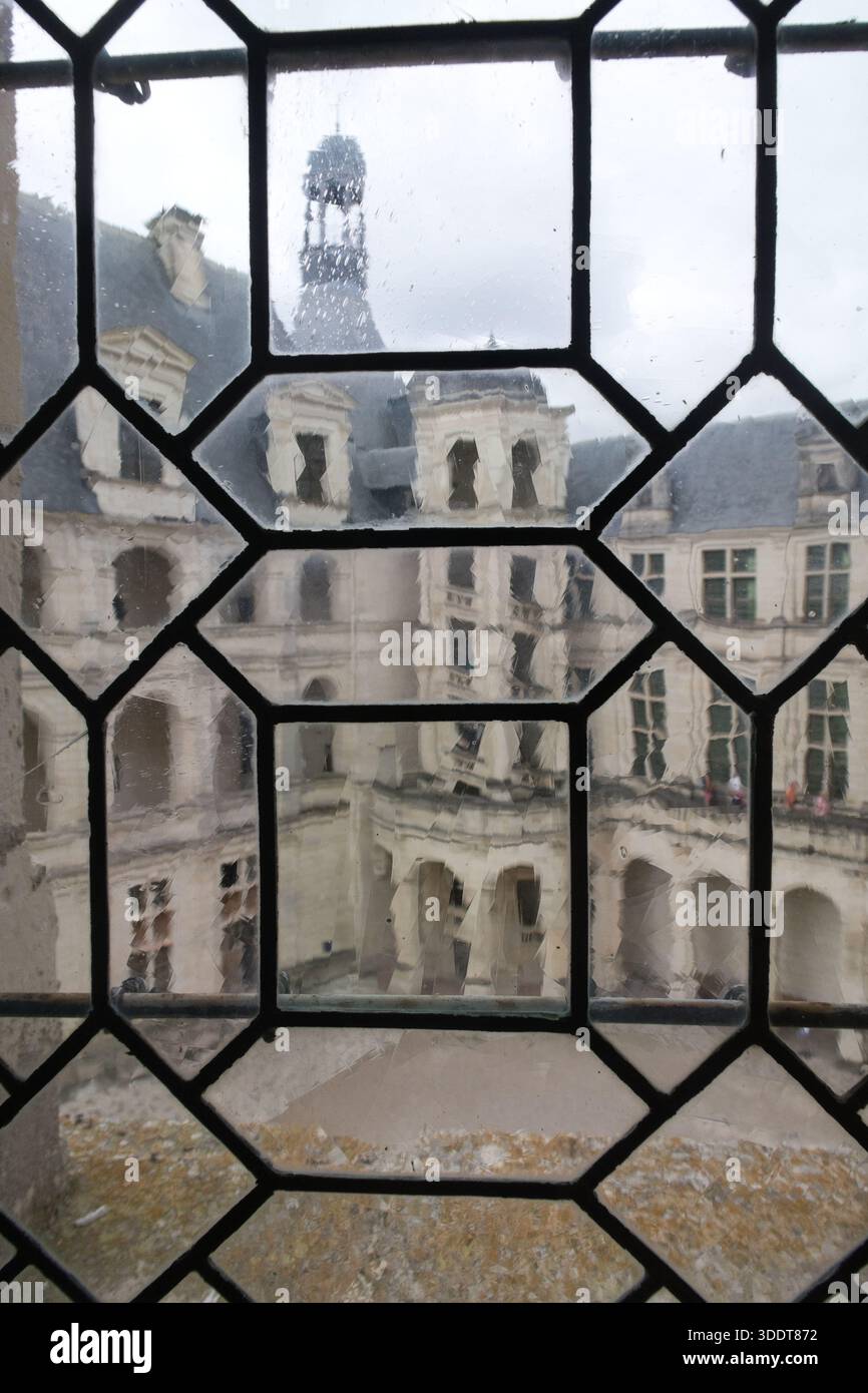 Chambord-Normandia-Francia - 16 luglio 2025, veduta di uno storico cortile e facciata di un castello francese visti attraverso un'antica finestra di vetro con struttura in piombo Foto Stock