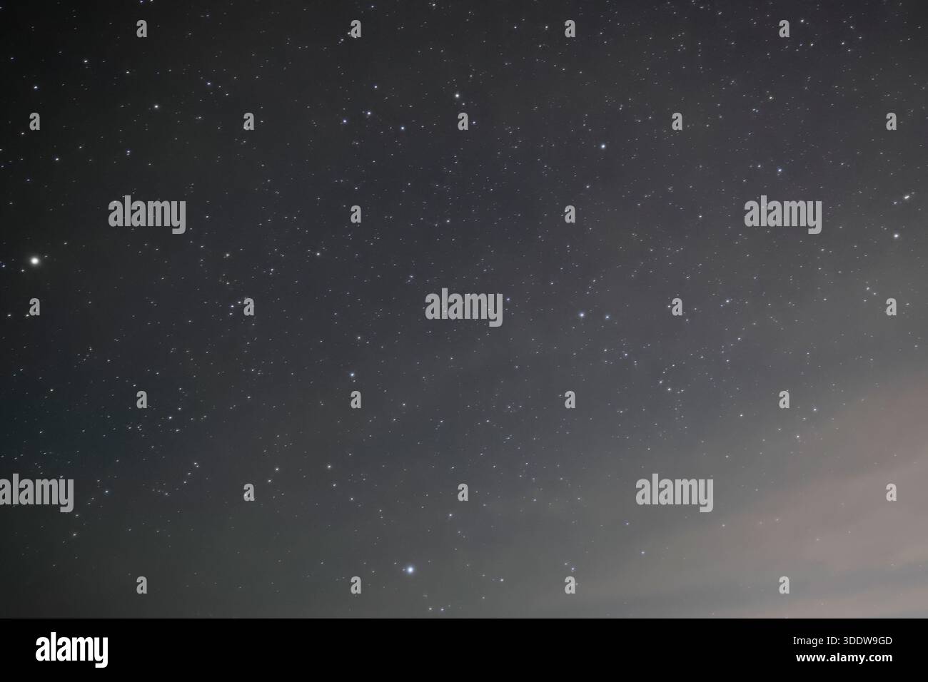 Un fitto campo di stelle e una debole nuvola si stagliano nel cielo notturno sopra il deserto sopra Sedona, Arizona, Stati Uniti, con un bagliore morbido vicino al bordo inferiore. Foto Stock