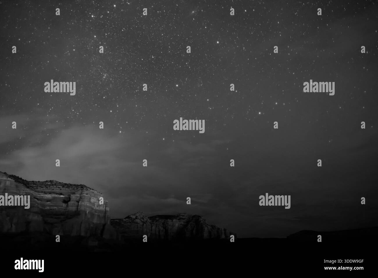 Campo stellare sopra scogliere di arenaria a strati e copertura nuvolosa alla deriva vicino a Sedona, Arizona, Stati Uniti, con un basso orizzonte desertico in primo piano. Foto Stock