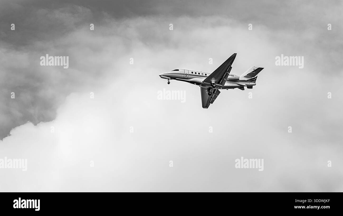 Un business jet Cessna Citation Latitude vola contro un cielo nuvoloso, catturato in bianco e nero. Foto Stock