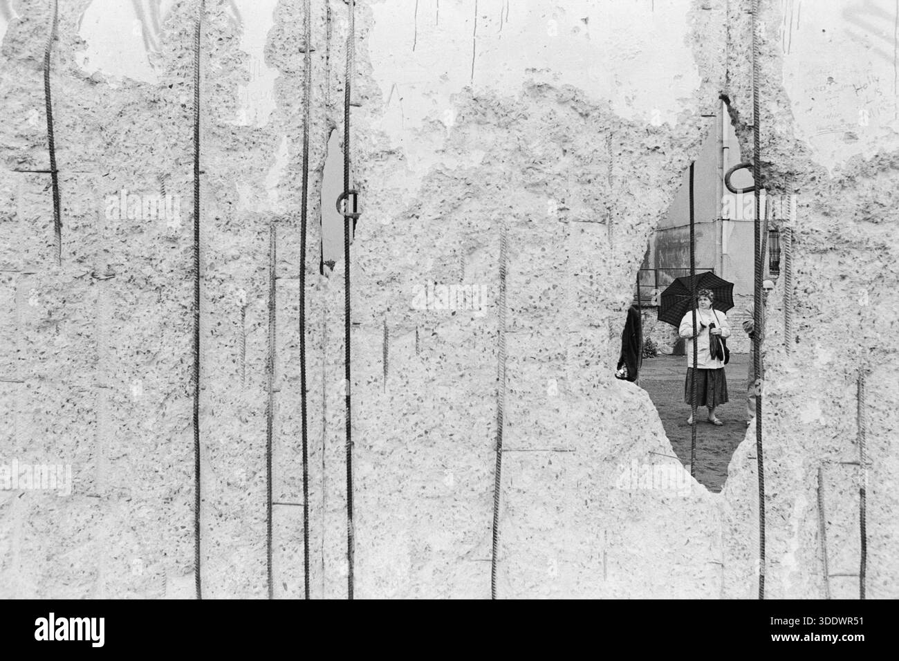 1990 Berlino Est, Germania: Foto in bianco e nero di una donna incorniciata attraverso un buco nel muro di Berlino in rovina durante l'era della riunificazione tedesca. Foto Stock