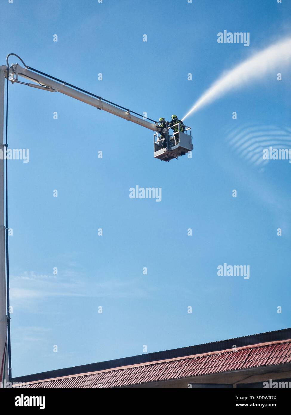 Sparatutto d'azione di due pompieri in un cestello della gru con un tubo flessibile ad alta pressione - attrezzatura per estinguere incendi ad alta quota. Foto Stock