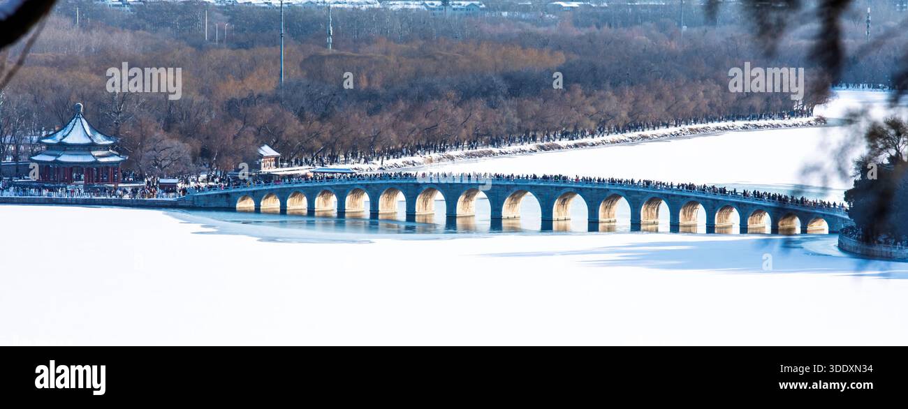I turisti attraversano a piedi il ponte del diciassettesimo arco presso il Palazzo d'Estate di Pechino, mentre il lago Kunming giace ghiacciato e coperto di neve. Foto Stock