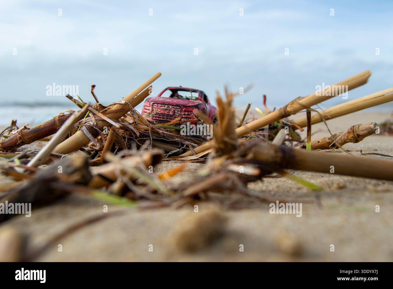 una piccola macchinetta rossa si trova tra le cime della spiaggia, ricordando ricordi dell'infanzia e momenti tranquilli del mare Foto Stock