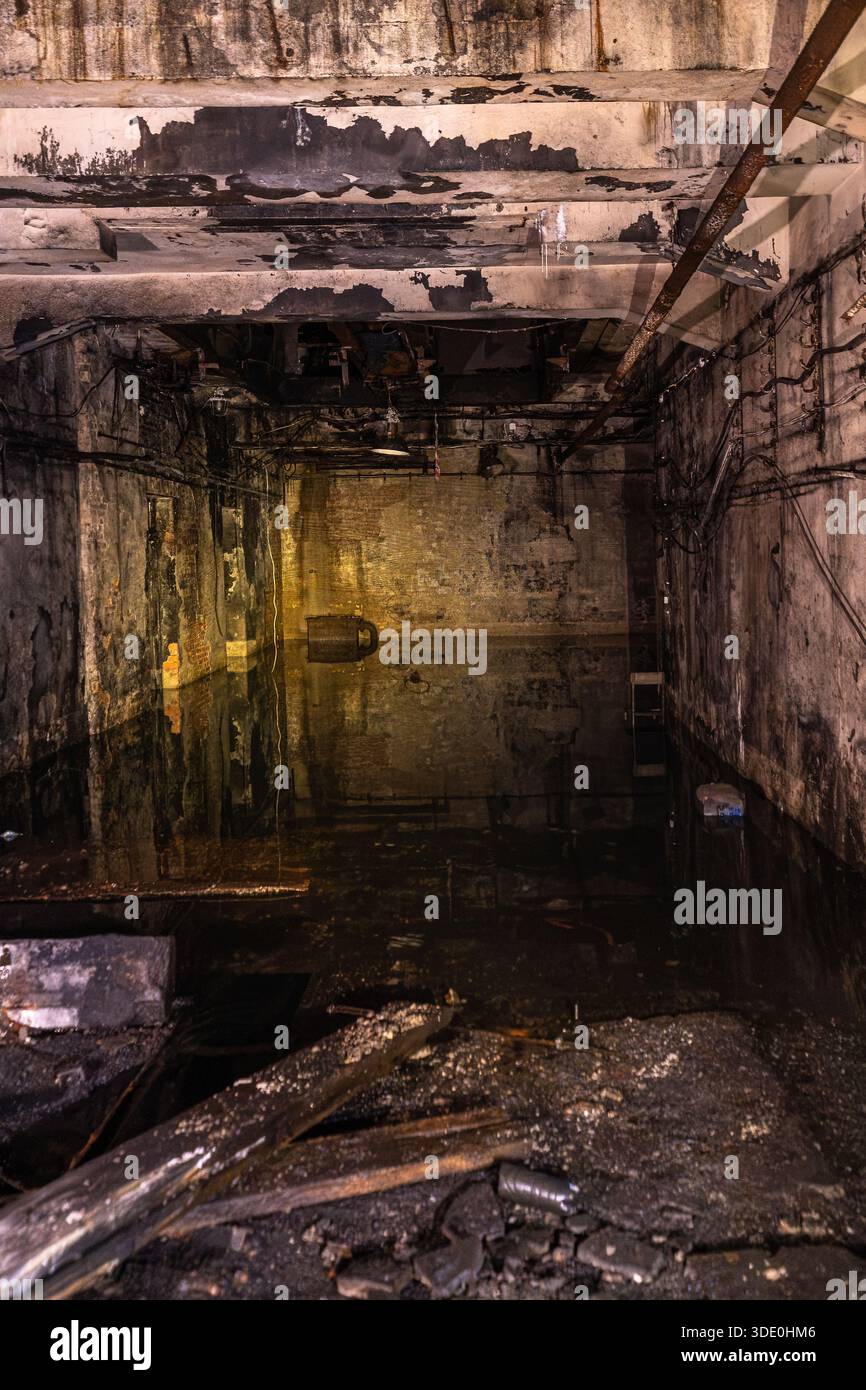 Grande camera industriale abbandonata con acqua stagnante superfici in calcestruzzo deteriorate e installazioni tecniche esposte Foto Stock
