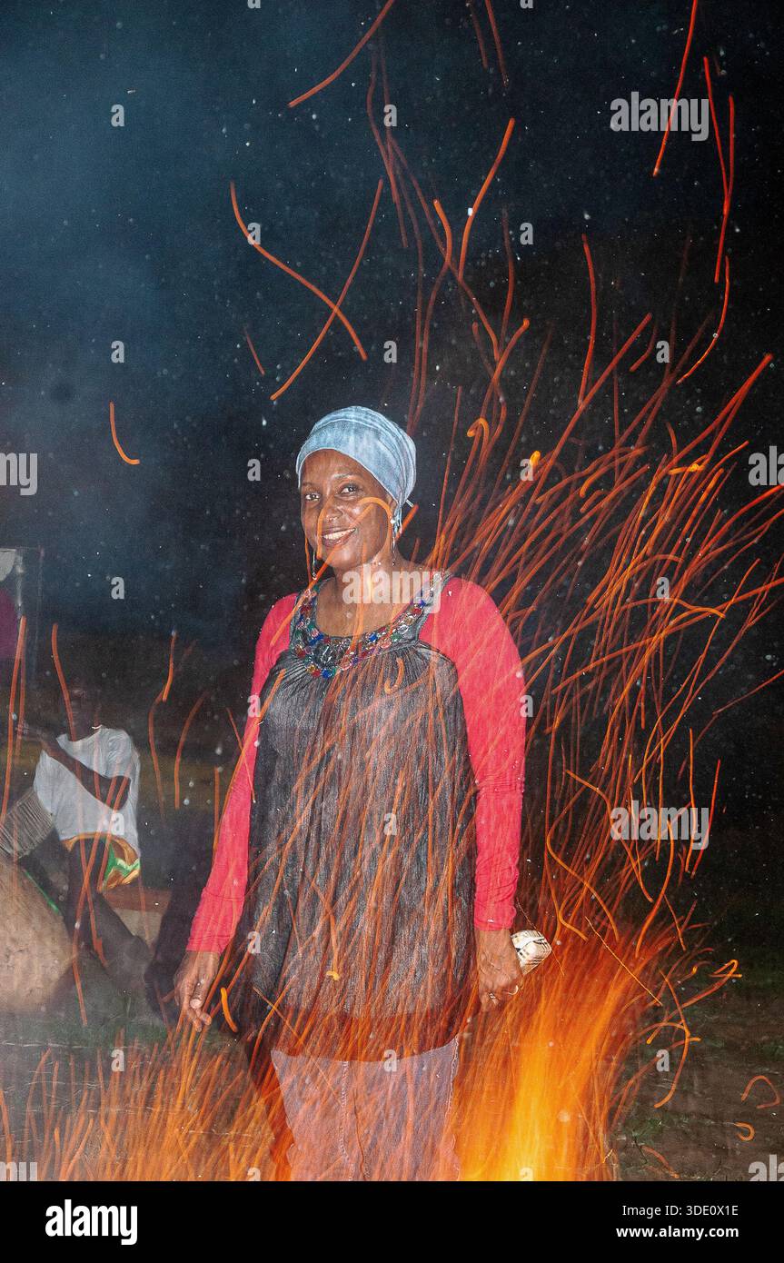 Un visitatore intorno al falò al Kyobe Safari Lodge, Murchison Falls, immerso nelle scintille tremolanti, godendosi una magica serata nella natura selvaggia dell'Uganda Foto Stock