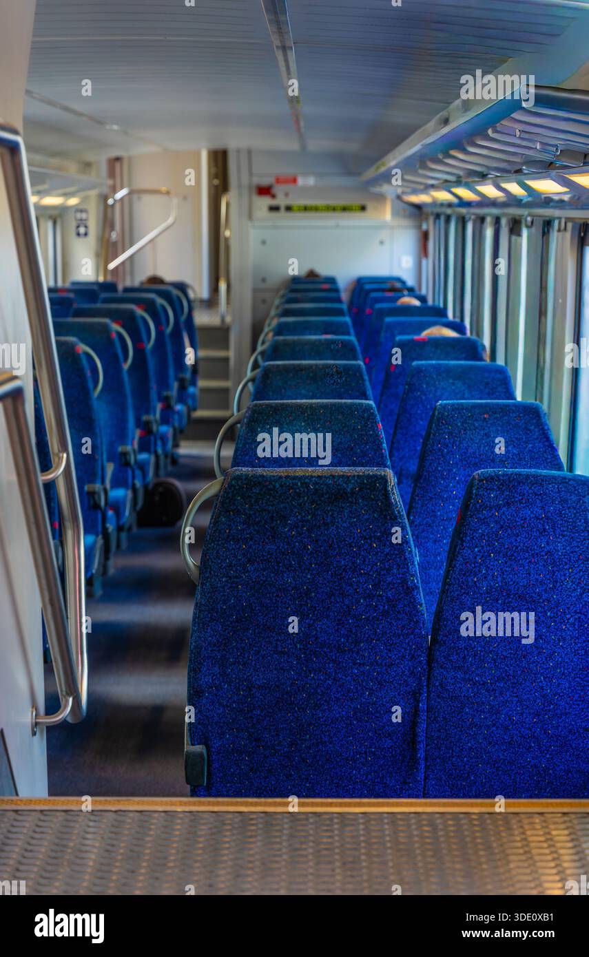 Ripresa verticale a livello degli occhi grandangolare dalle scale che guardano in basso alla corsia di una cabina ferroviaria per pendolari pulita e luminosa con un morbido sedile blu per passeggeri Foto Stock