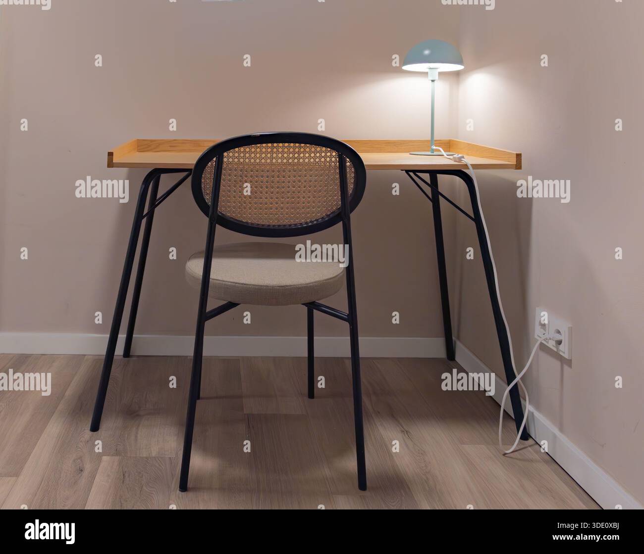 Scatto orizzontale grandangolare che mostra uno spazio di lavoro in legno pulito contro una parete neutra, con un'elegante lampada da scrivania e mobili ergonomici Foto Stock