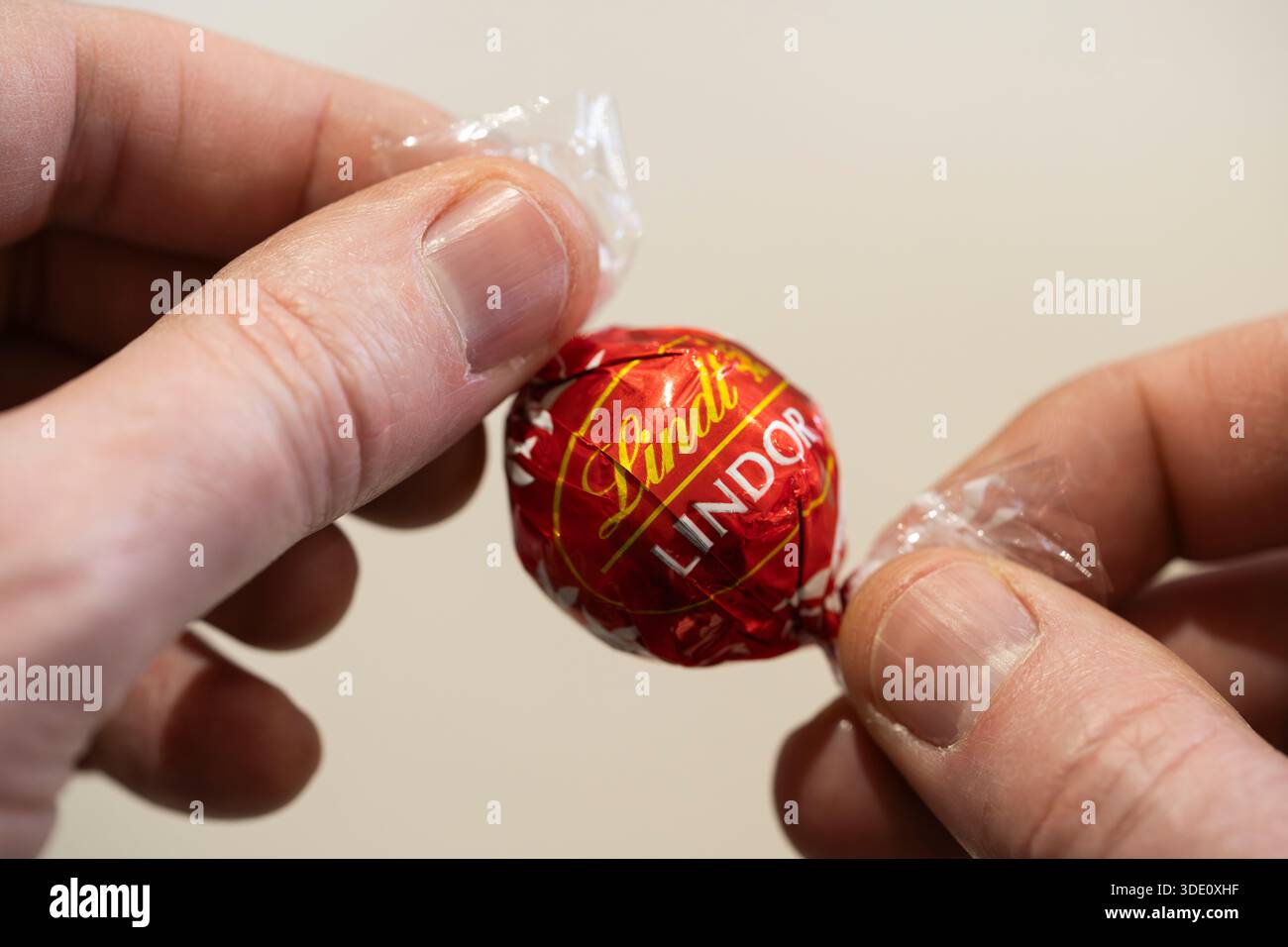 Uomo che tiene e svuota il tartufo Lindor al cioccolato al latte dell'azienda svizzera di cioccolato e dolciumi, Lindt. REGNO UNITO. Concetto: Prezzo del cacao, costo della vita Foto Stock